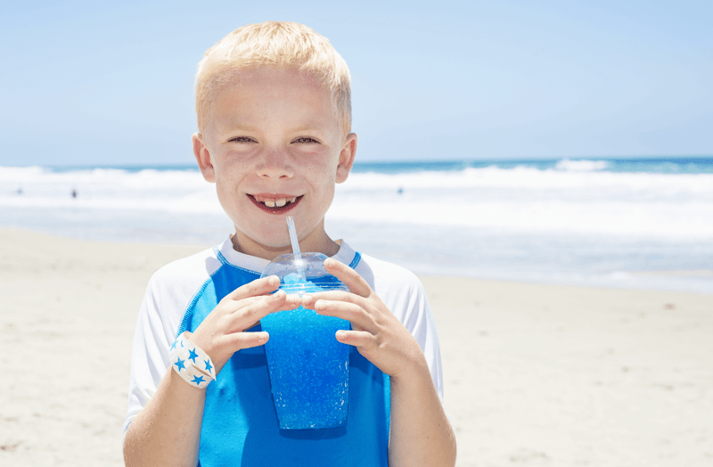 FBD Frozen. A young child drinks a blue frozen beverage on the beach.